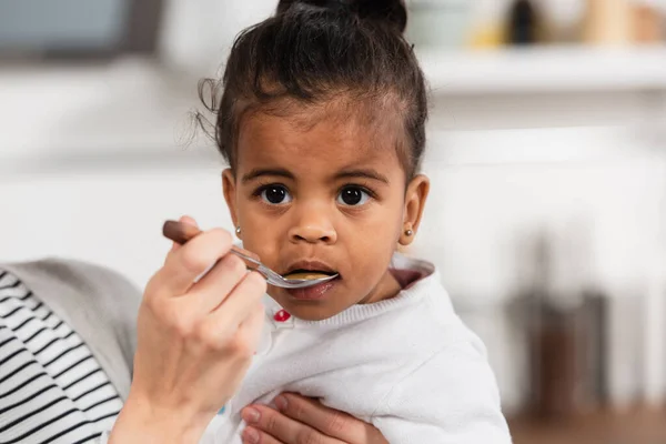 Mother holding spoon and feeding adopted african american daughter — Stock Photo