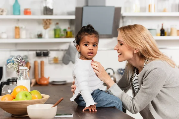 Glückliche Mutter blickt auf adoptiertes afrikanisches amerikanisches Kind in Küche — Stockfoto