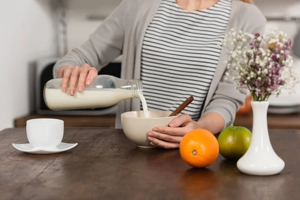 Vue partielle de la femme versant du lait dans un bol — Photo de stock