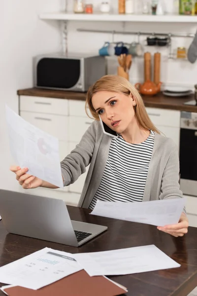 Blonde pigiste parler sur téléphone portable et détenir des documents tout en travaillant à la maison — Photo de stock