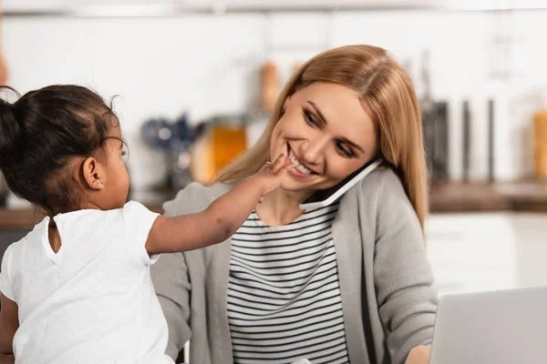 Happy mother talking on smartphone near adopted african american kid with outstretched hand — Stock Photo