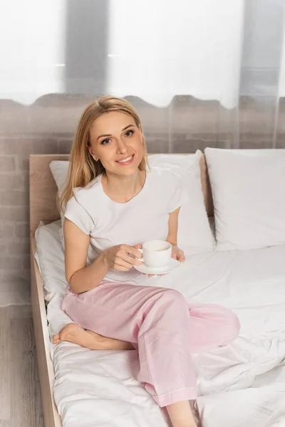 Donna felice in pigiama con in mano una tazza di caffè in camera da letto — Foto stock