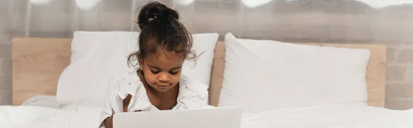 Niño afroamericano feliz del niño usando el ordenador portátil en dormitorio, bandera - foto de stock