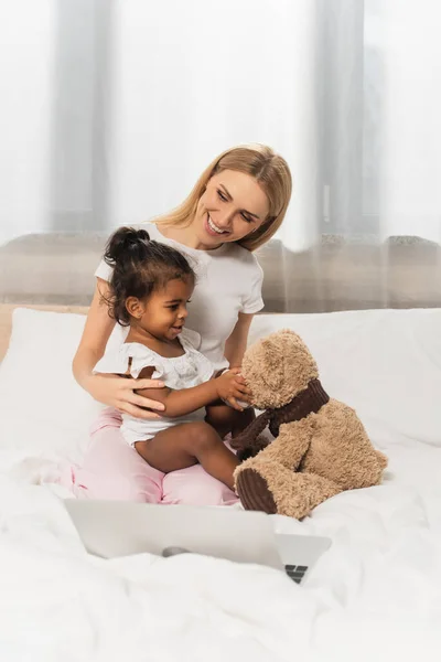 Fröhliche Mutter umarmt adoptiertes afrikanisches Kind mit Teddybär — Stockfoto
