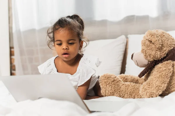 Étonné afro-américain enfant regarder film sur ordinateur portable près de jouet mou — Photo de stock