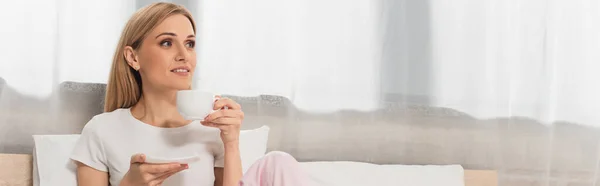 Femme blonde souriante tenant une tasse de café dans la chambre, bannière — Photo de stock