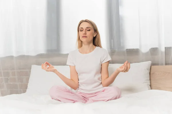 Femme blonde en pyjama méditant sur le lit — Photo de stock