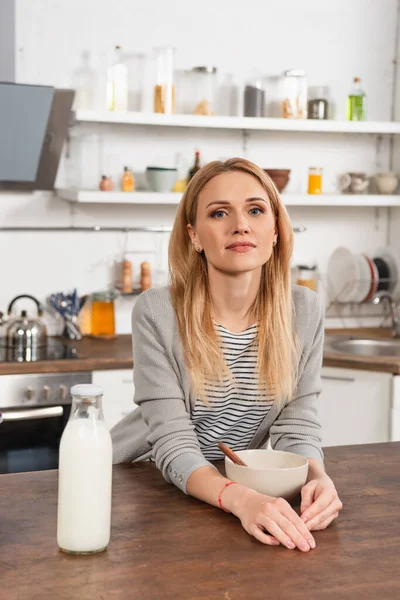 Blonde woman looking at camera near bowl bottle of milk — Stock Photo