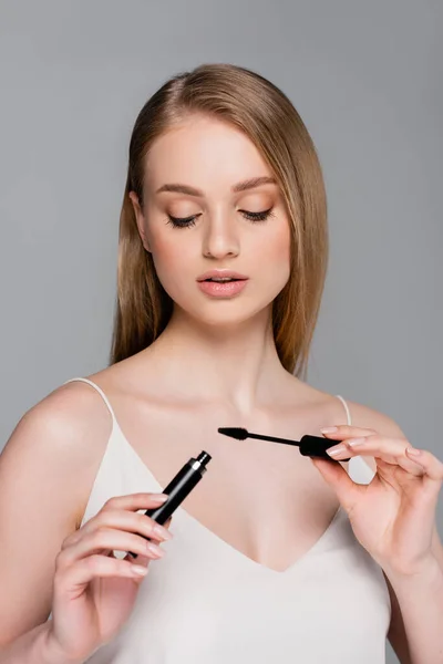 Young woman holding tube with mascara and brush isolated on grey — Stock Photo