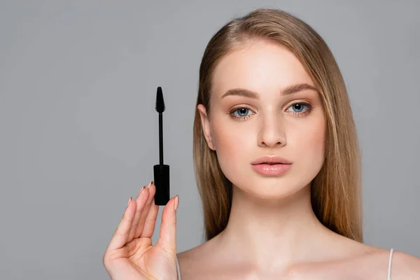 Young woman holding brush with black mascara isolated on grey — Stock Photo