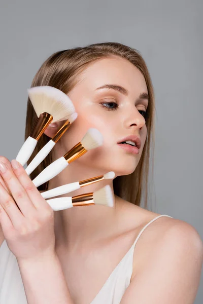 Young woman holding set of different cosmetic brushes isolated on gray — Stock Photo