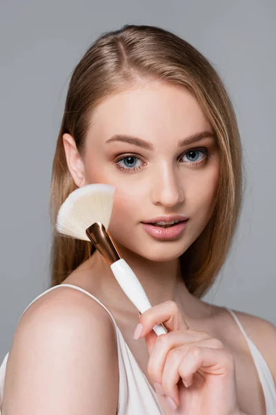 Young and pretty woman holding cosmetic brush isolated on grey — Stock Photo