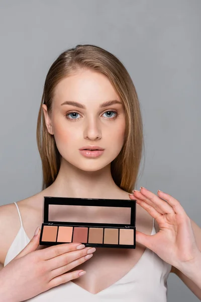 Jolie femme tenant la palette de fard à joues cosmétique isolé sur gris — Photo de stock