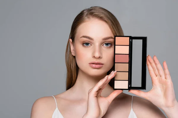 Young pretty woman holding cosmetic blush palette isolated on grey — Stock Photo