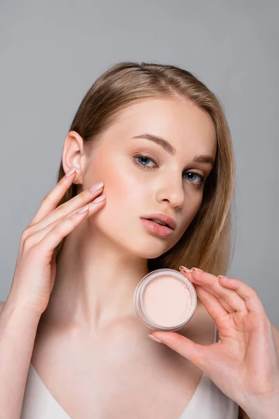 Pretty blonde woman holding container with face powder isolated on grey — Stock Photo