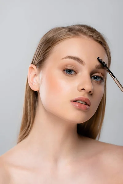 Pretty woman with bare shoulders styling eyebrow isolated on grey — Stock Photo