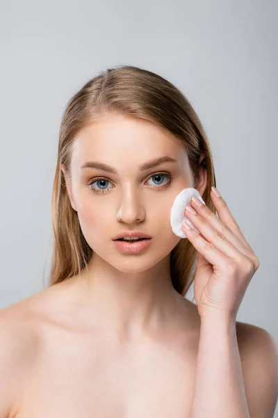 Young woman with blue eyes removing makeup with cotton pad isolated on grey — Stock Photo