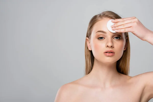 Pretty woman with bare shoulders removing makeup with cotton pad isolated on grey — Stock Photo