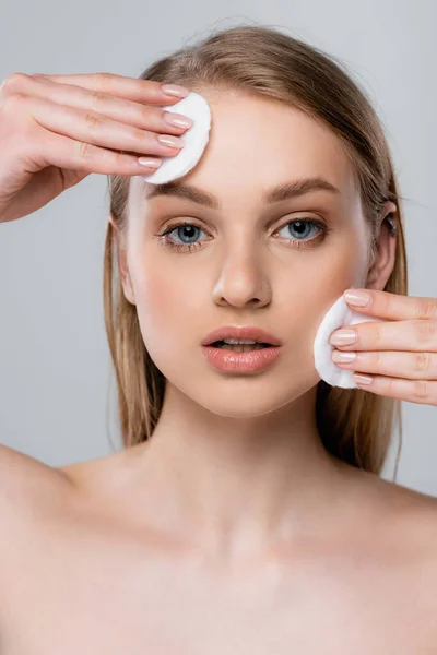 Mujer joven con ojos azules quitando maquillaje con almohadillas de algodón aisladas en gris - foto de stock