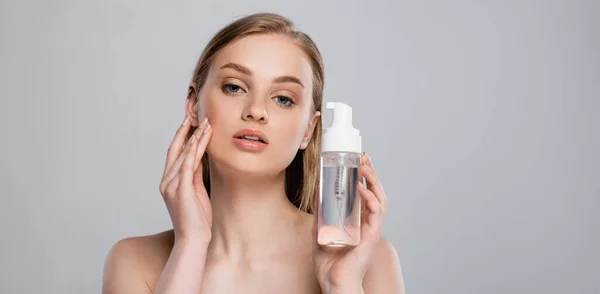 Hübsche junge Frau mit nackten Schultern, die Flasche mit mikellerem Wasser auf grau isoliert hält, Banner — Stockfoto