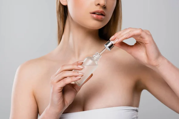 Abgeschnittene Ansicht einer Frau mit nackten Schultern, die Flasche mit Serum und Pipette isoliert auf grau hält — Stockfoto