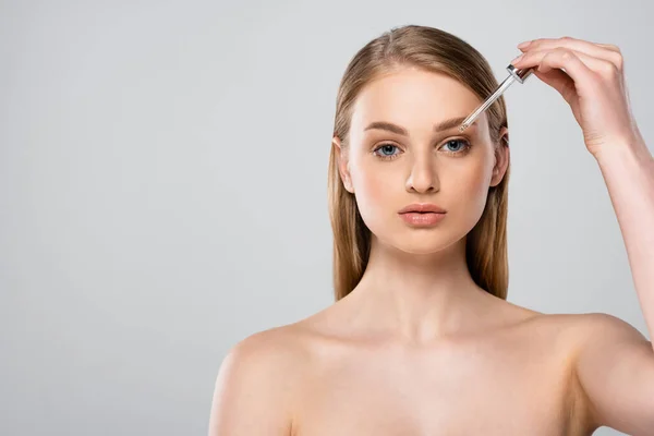 Jolie femme aux yeux bleus appliquant sérum avec pipette isolée sur gris — Photo de stock