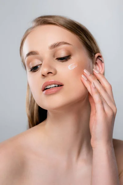 Pretty woman applying cream on face isolated on grey — Stock Photo