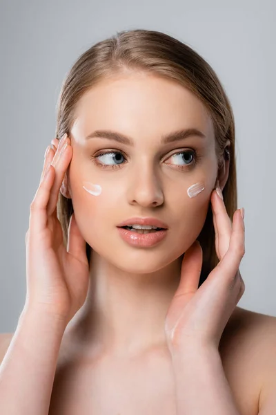 Bonita mujer aplicando crema facial aislada en gris - foto de stock