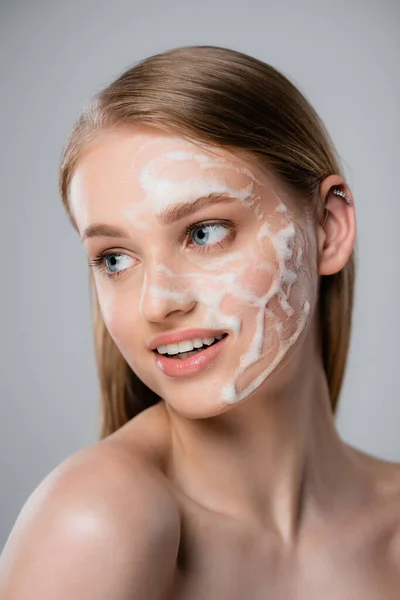 Giovane donna con occhi azzurri e schiuma detergente sul viso isolata su grigio — Foto stock