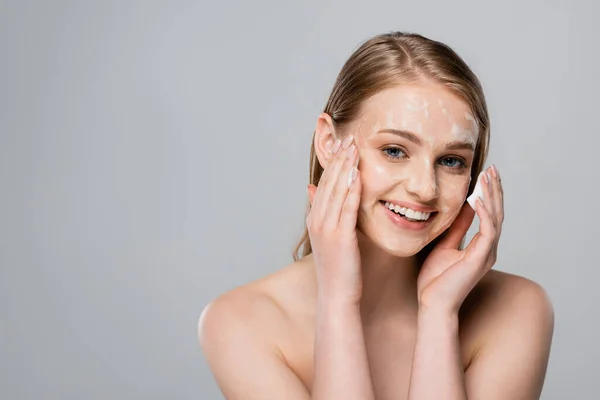 Happy young woman with blue eyes and cleansing foam on face isolated on grey — Stock Photo