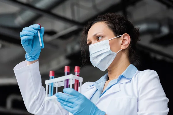 Vue à faible angle du scientifique afro-américain dans un masque médical tenant des éprouvettes — Photo de stock