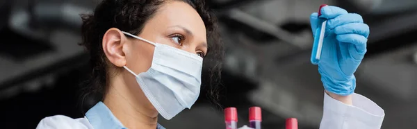 Visão de baixo ângulo do cientista afro-americano em máscara médica olhando para tubo de teste, banner — Fotografia de Stock