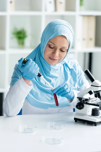 Muslim scientist working with electronic pipette and blood sample near microscope — Stock Photo