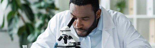 African american scientist looking through microscope in lab, banner - foto de stock