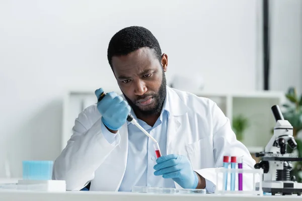 Cientista afro-americano em luvas de látex segurando tubo de ensaio e pipeta eletrônica em laboratório — Fotografia de Stock