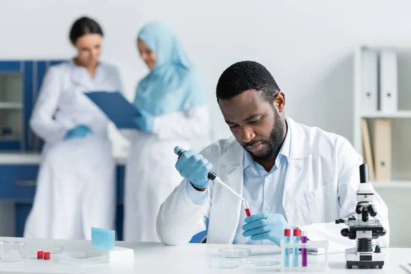 African american scientist researching samples in test tubes near blurred colleagues in lab — Stock Photo