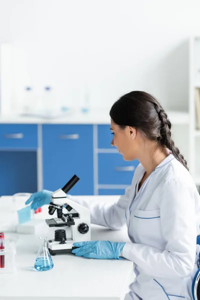 Side view of scientist working in laboratory with microscope and flask — Stock Photo