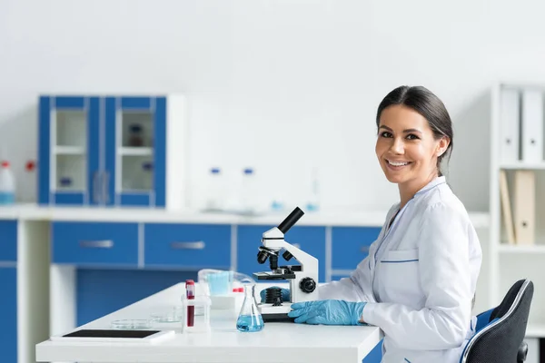 Scientist smiling at camera near digital tablet and medical equipment in lab - foto de stock