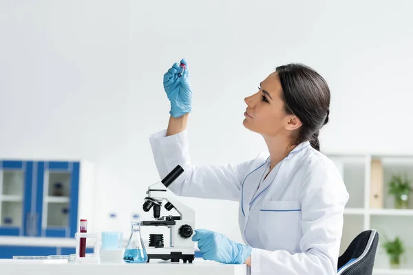 Side view of scientist in white coat looking at test tube near medical equipment - foto de stock