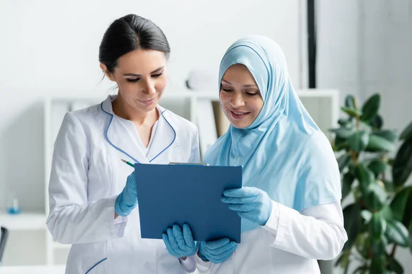 Sorridente medico arabo che tiene appunti vicino collega — Foto stock