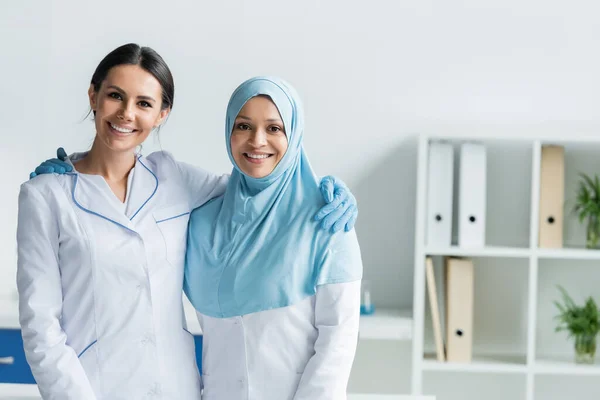 Médecins multiethniques souriant et regardant la caméra dans la clinique — Photo de stock