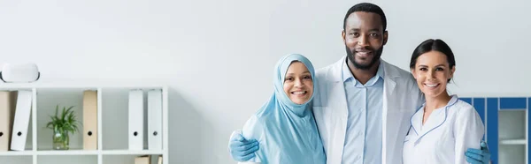 Médecin afro-américain étreignant ses collègues souriants à la clinique, bannière — Photo de stock