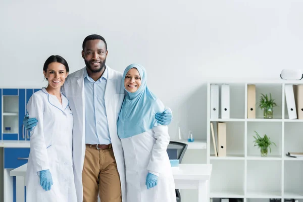 African american scientist in latex gloves hugging colleagues in lab — Stock Photo
