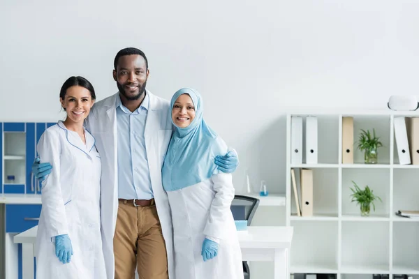 African american scientist in latex gloves hugging colleagues in lab - foto de stock