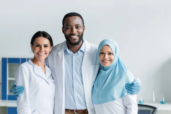 Cheerful multicultural scientists hugging in laboratory — Stock Photo