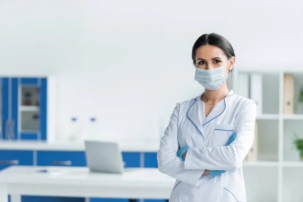 Врач в латексных перчатках и медицинской маске стоит со скрещенными руками в больнице — стоковое фото