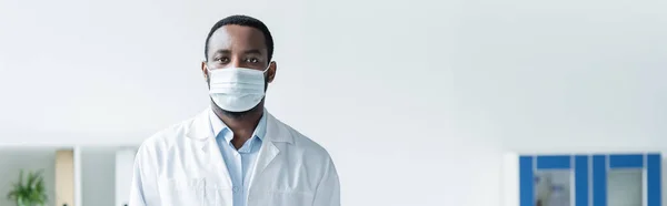 Medico afroamericano in maschera medica in piedi in clinica, striscione — Foto stock
