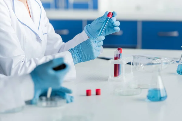 Ausgeschnittene Ansicht eines Wissenschaftlers, der Reagenzglas in der Nähe verschwommener Kollegen hält, die im Labor arbeiten — Stockfoto