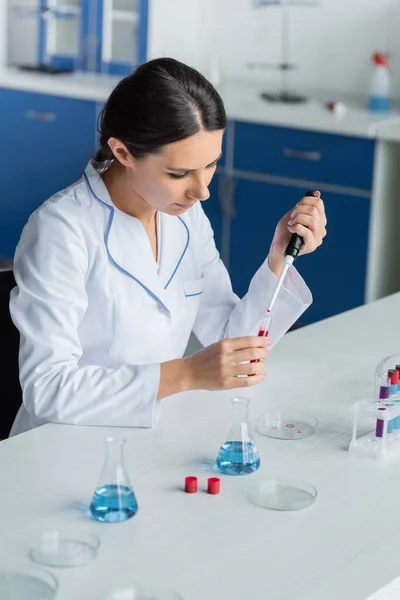 Scientist holding blood sample and electronic pipette near flasks — Stock Photo