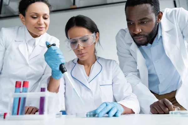 African american scientists standing near colleague with pipette and test tubes - foto de stock
